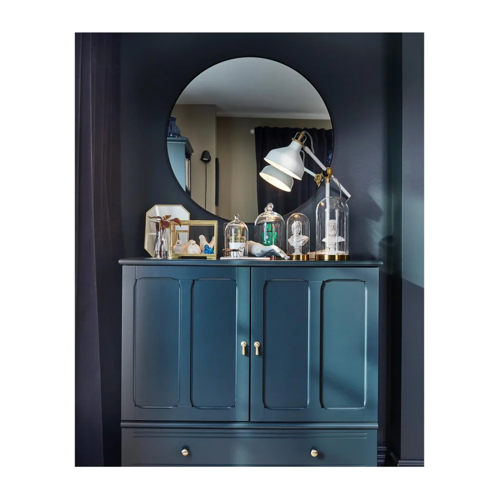 Specchio rotondo LINDBYN con cornice nera sopra una credenza.