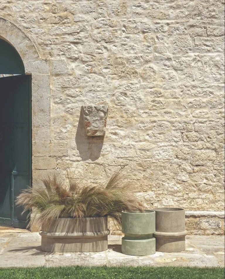 Composizione di vasi Ethimo verdi e grigi con vegetazione davanti a un muro in pietra