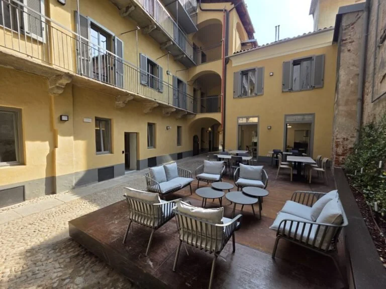 Corte di The Yard a Biella con sedute, tavolini e finestre sullo spazio condiviso