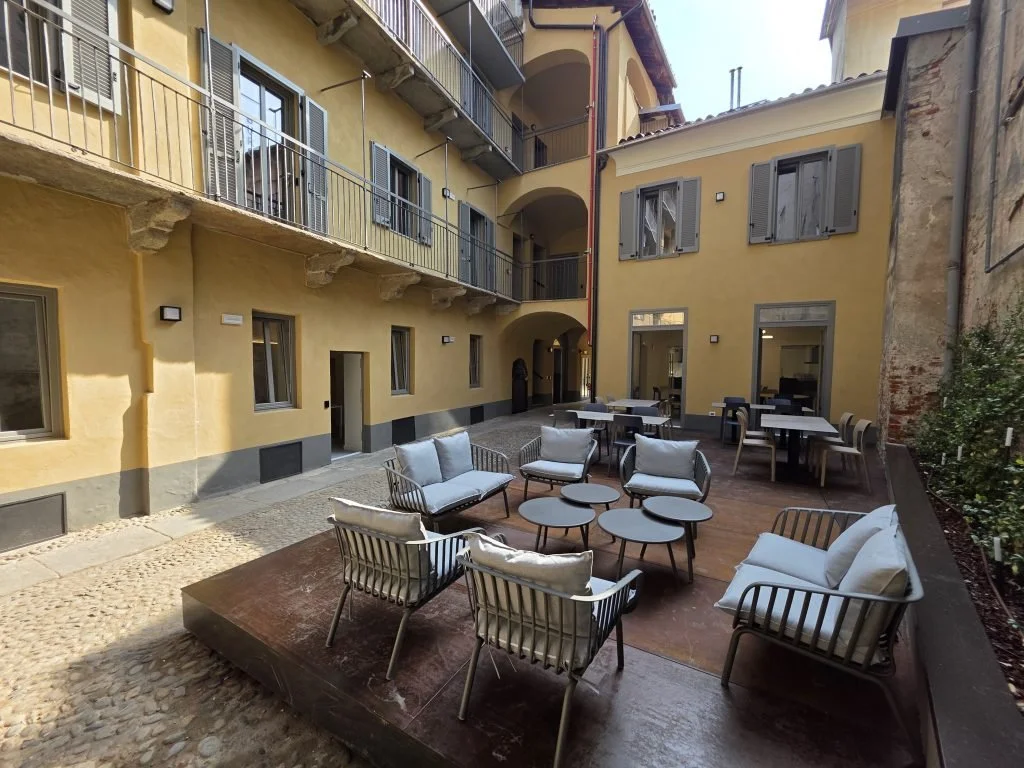 Corte di The Yard a Biella con sedute, tavolini e finestre sullo spazio condiviso